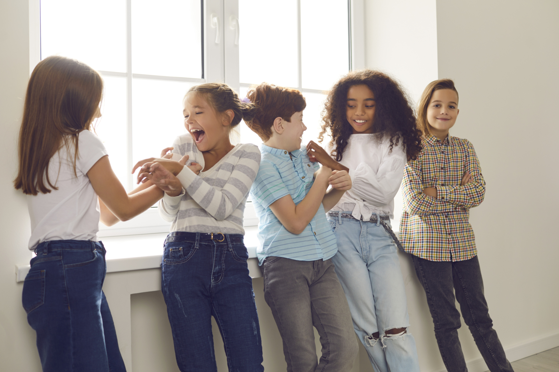 Group of happy diverse friends playing, tickling each other, laughing, having fun during school recess or party at home. Children's social interaction with peers, intercultural kids community concepts