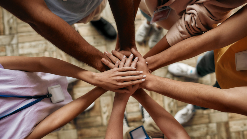 Top view of diverse young volunteers putting their hands on top of each other like a real team while standing in charitable organization office, Selective focus on hands, Web Banner